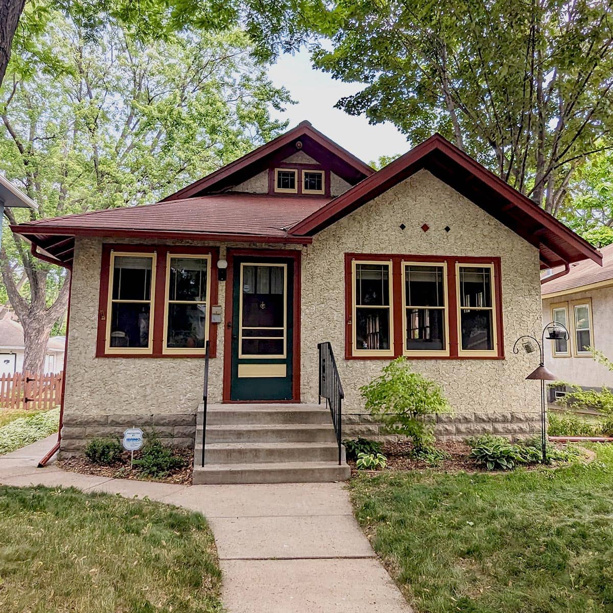 Charming bungalow with red trim, surrounded by lush trees.