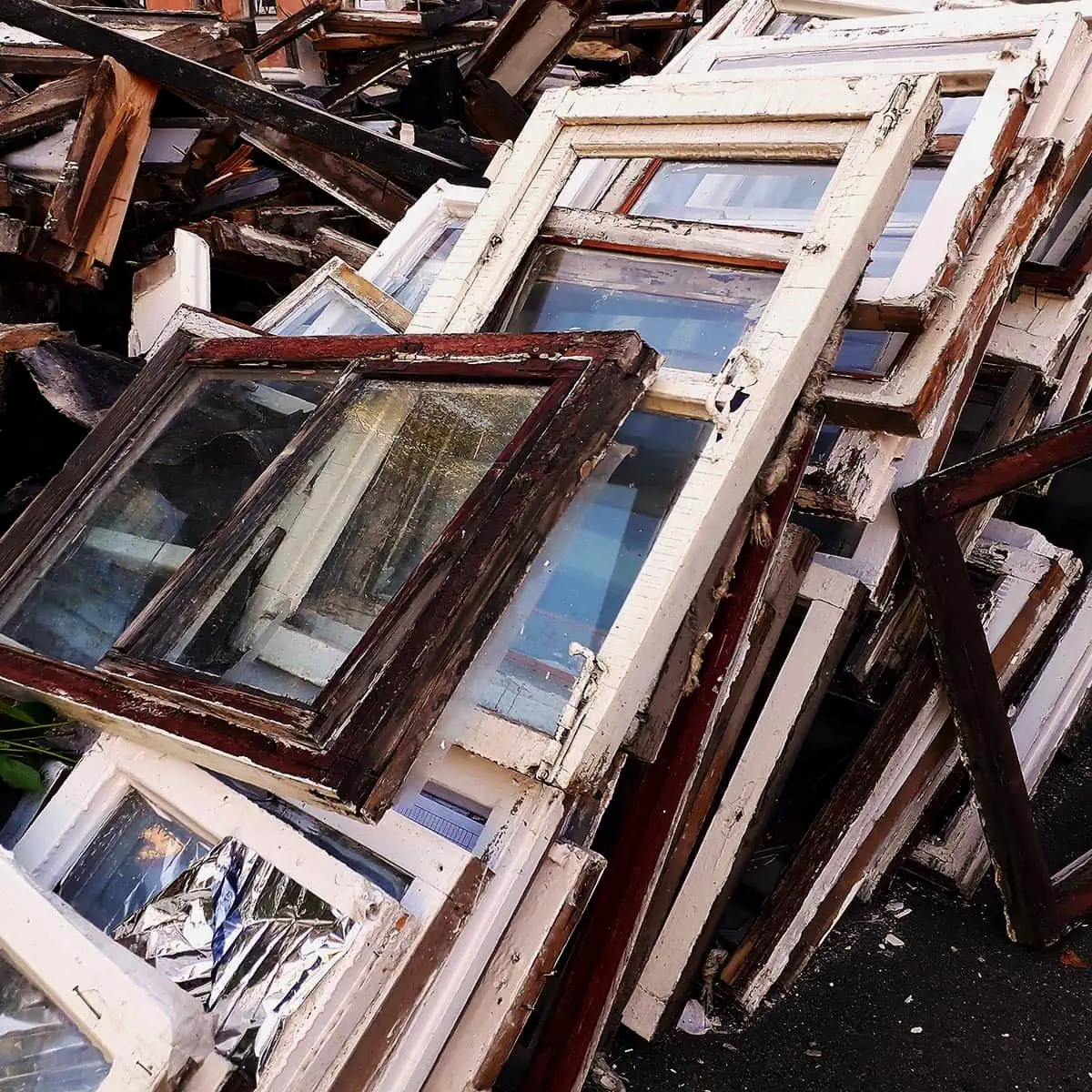 Hayes-Window-Restoration-Window-Trash-2-SQ Broken and weathered window frames stacked together, awaiting restoration or recycling.