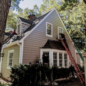Workers repairing roof and windows on suburban house.