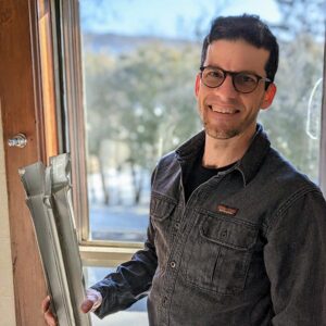 Smiling man holding architectural plans by window.