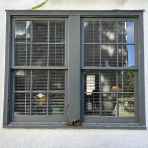 Large gray window with closed blinds and sunlight patterns.