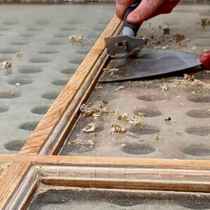 Hand scraping old varnish from wooden window frame.