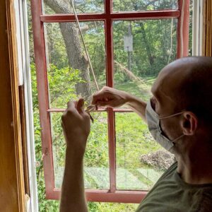 Man repairing red window frame, scenic outdoor backdrop.