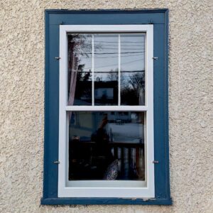 Blue-framed window on textured wall, reflecting trees.