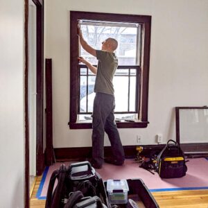 Man installing a window in a room, tools nearby.