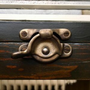Vintage brass window latch close-up on wooden frame.