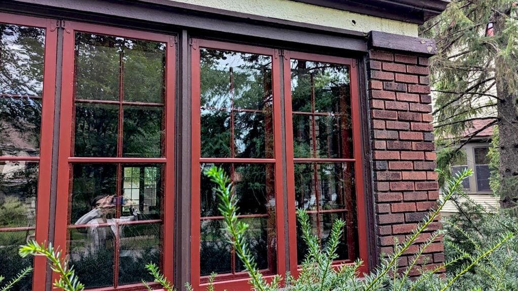 Red framed windows on brick building with greenery