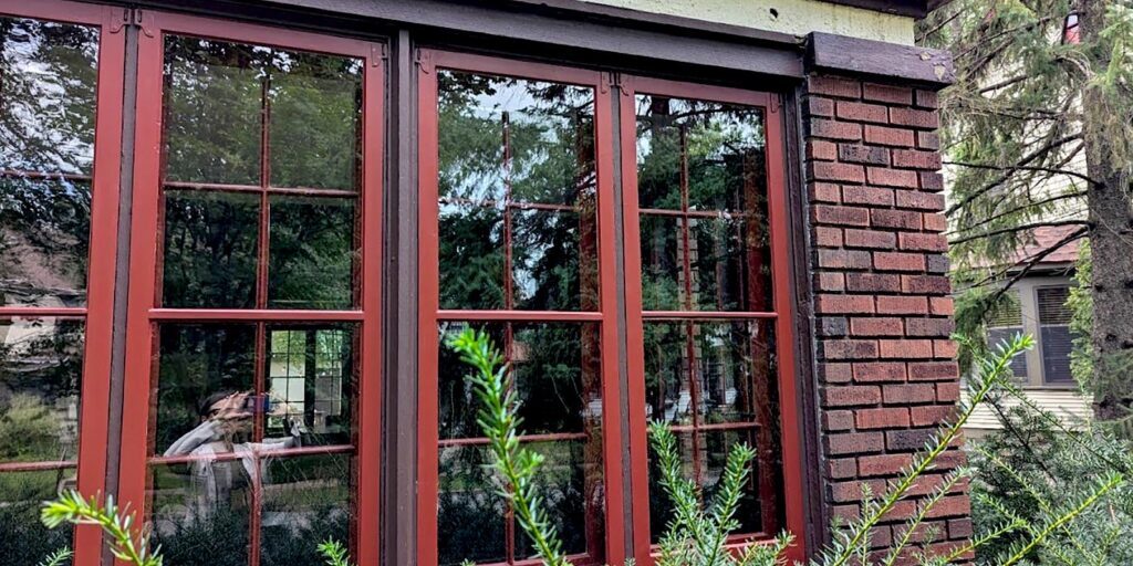 Red framed windows on brick building with greenery