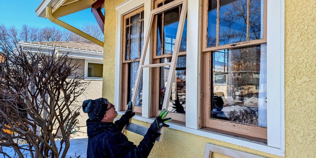 Worker installing new window in sunny winter setting.